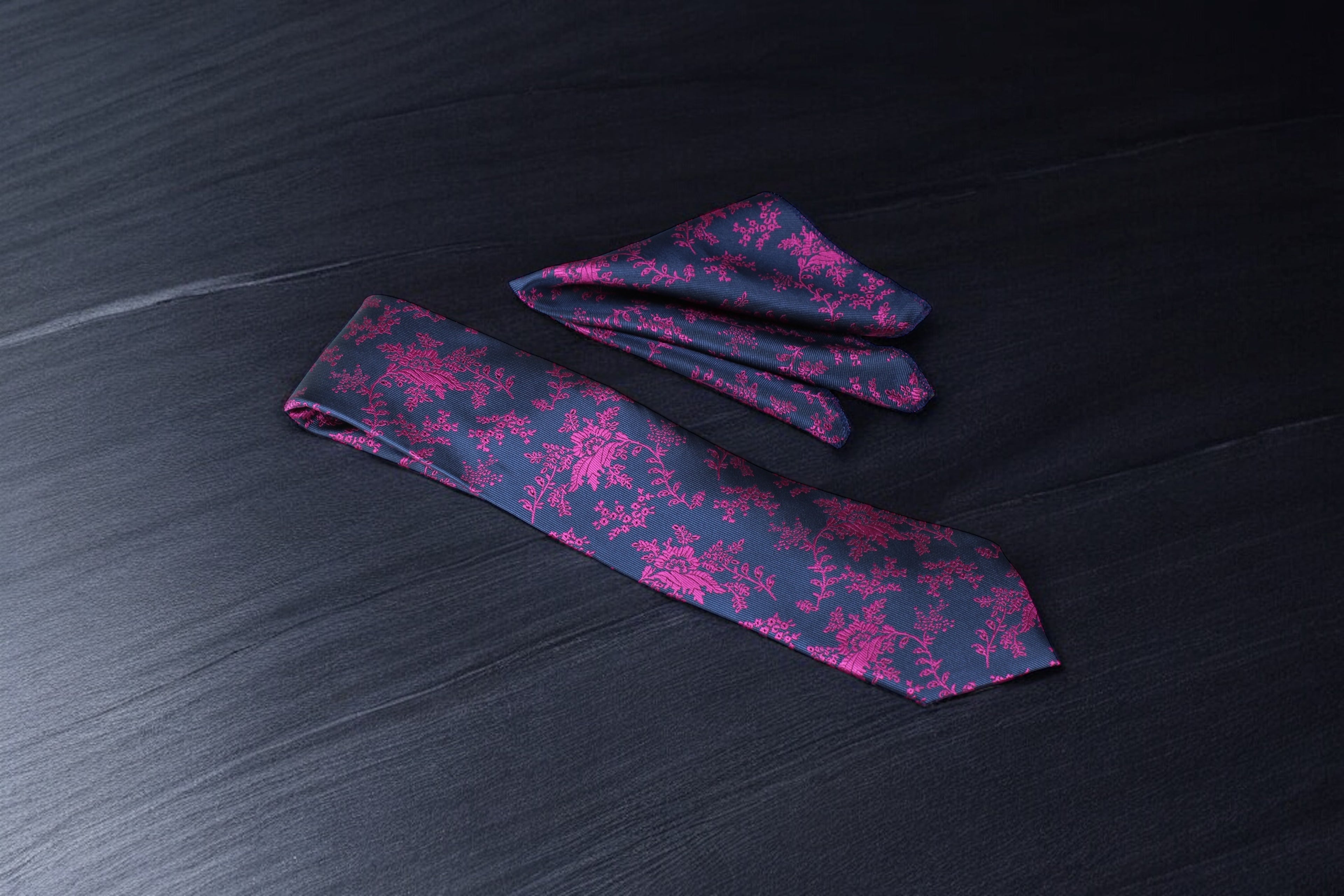A floral tie with blue and magenta colors laid out on a dark surface.