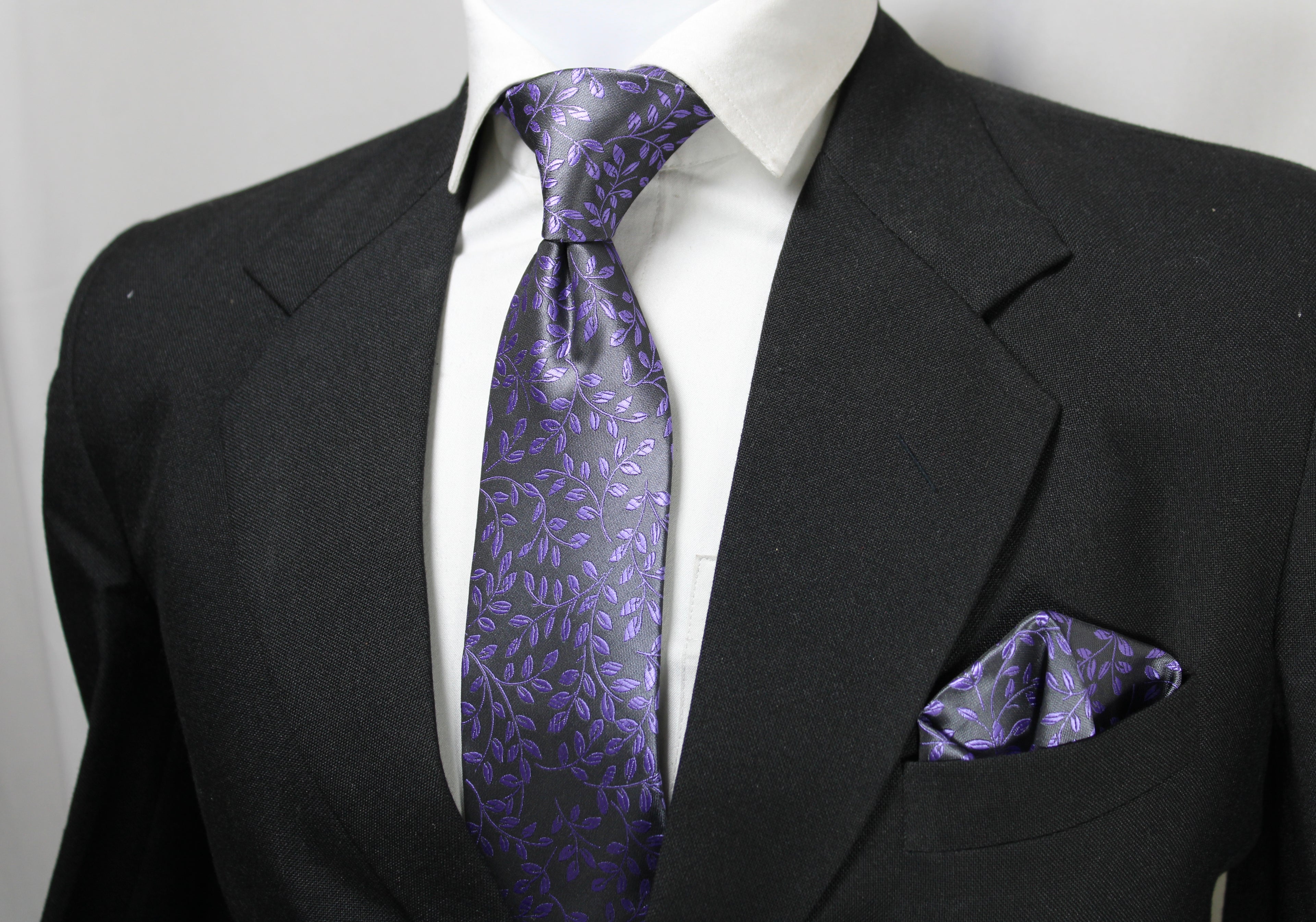 A mannequin wearing a black suit, displaying a gray and purple floral tie and a matching pocket square.