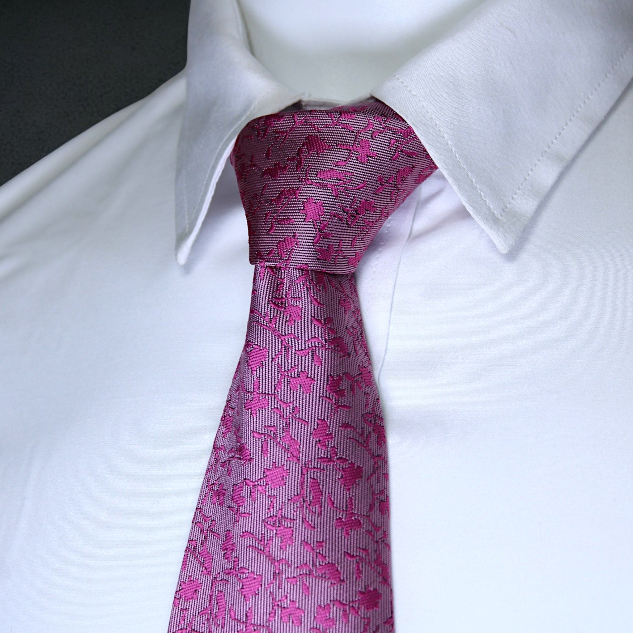 Close-up of a white shirt with a pink patterned tie against a neutral background