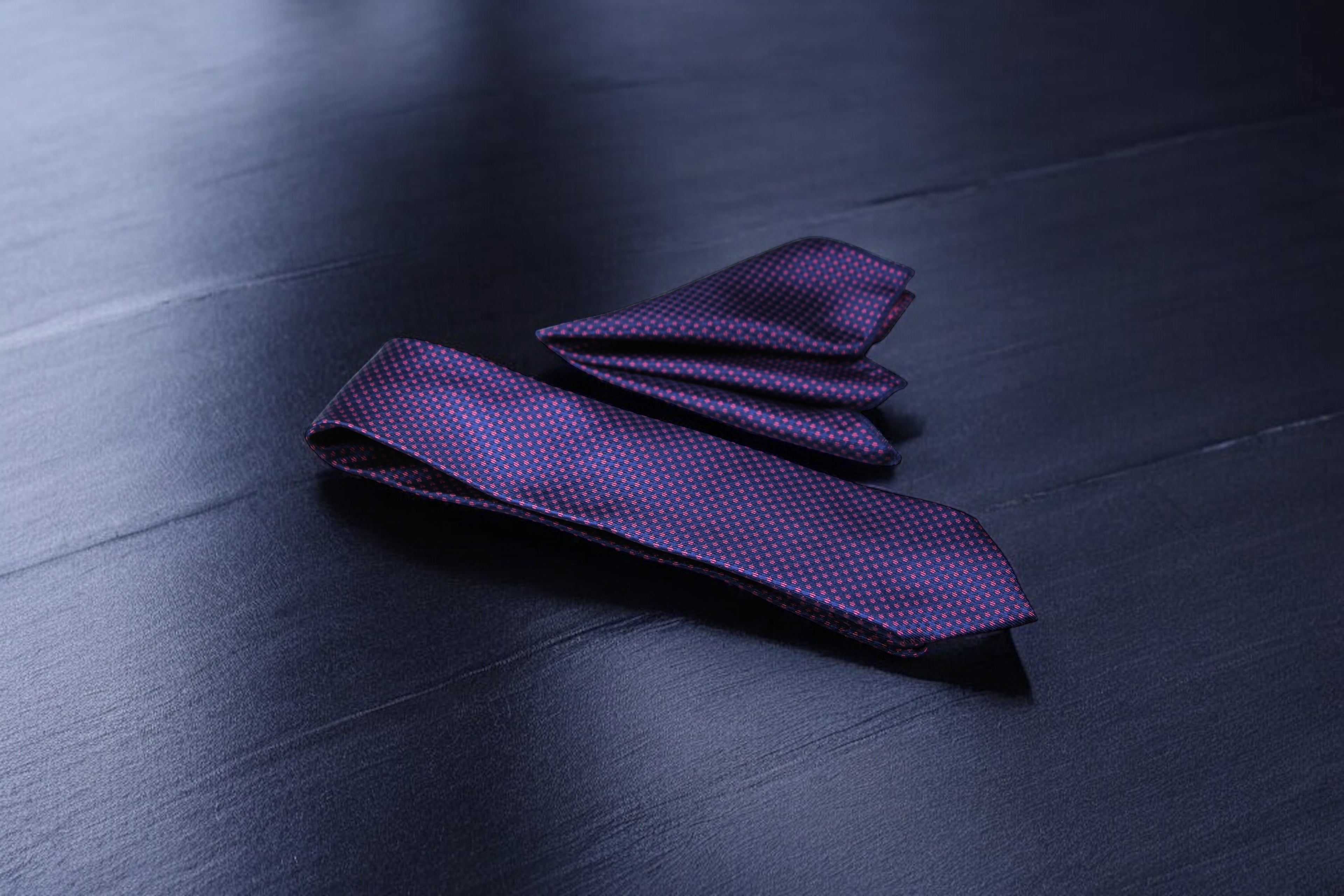 A dotted tie in blue and magenta colors spread out on a dark surface.