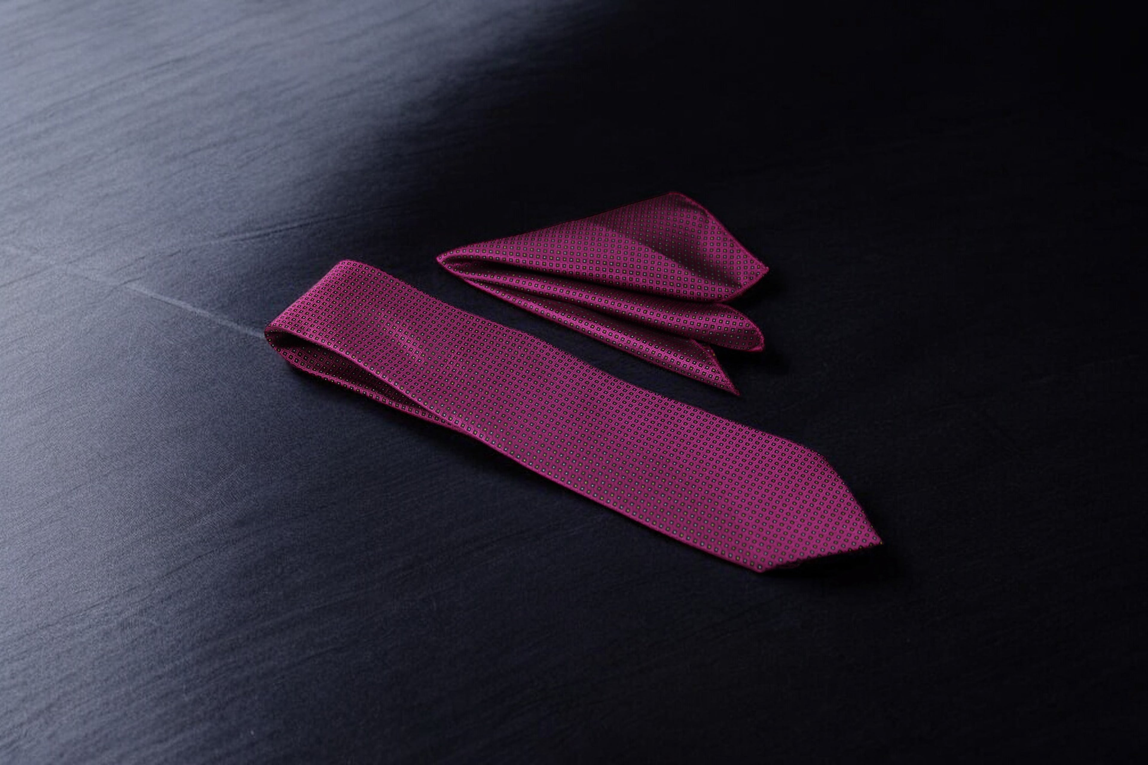 A magenta geometric tie and pocket square set laid out on a dark surface.