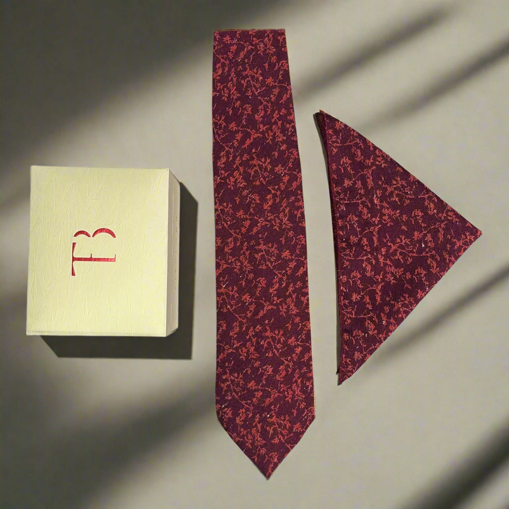 Red patterned tie and matching pocket square with a branded box on a neutral background