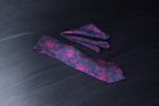 A floral tie with blue and magenta colors laid out on a dark surface.