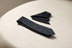 A black necktie and a pocket square with a floral pattern laid out on a surface.