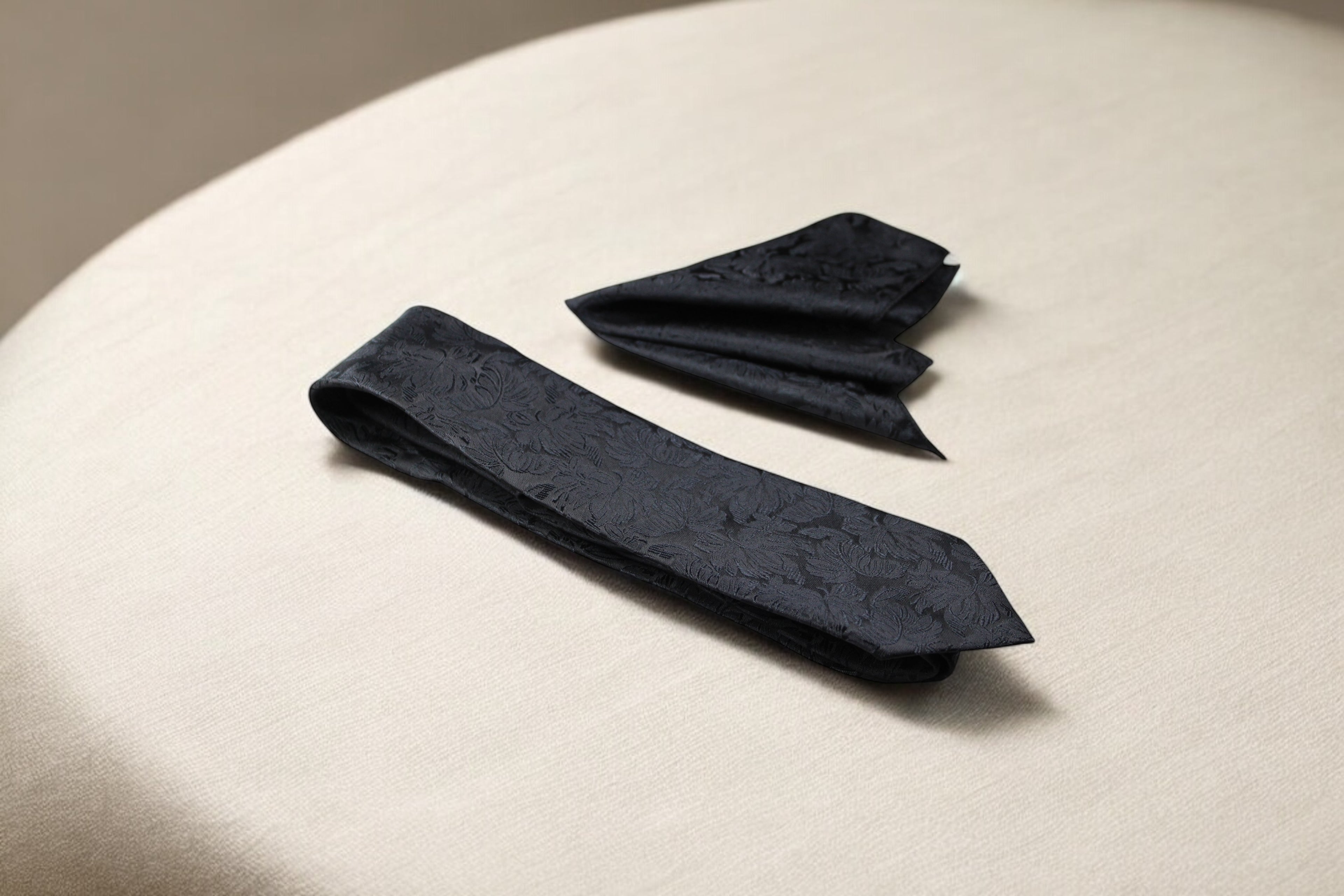 A black necktie and a pocket square with a floral pattern laid out on a surface.