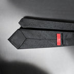 Black patterned tie with a red label on a gray background