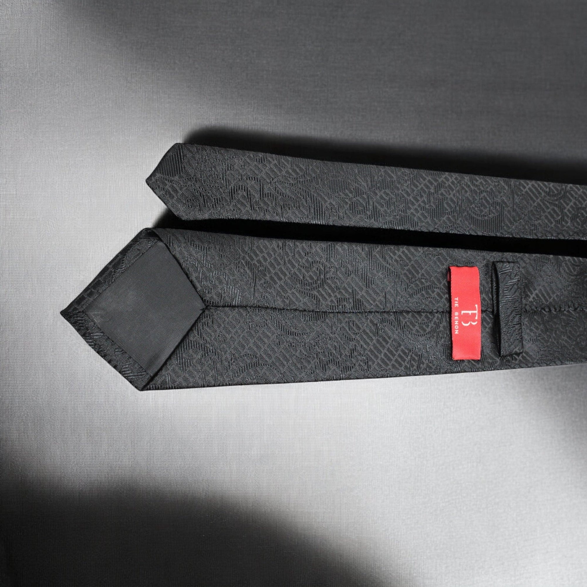 Black patterned tie with a red label on a gray background