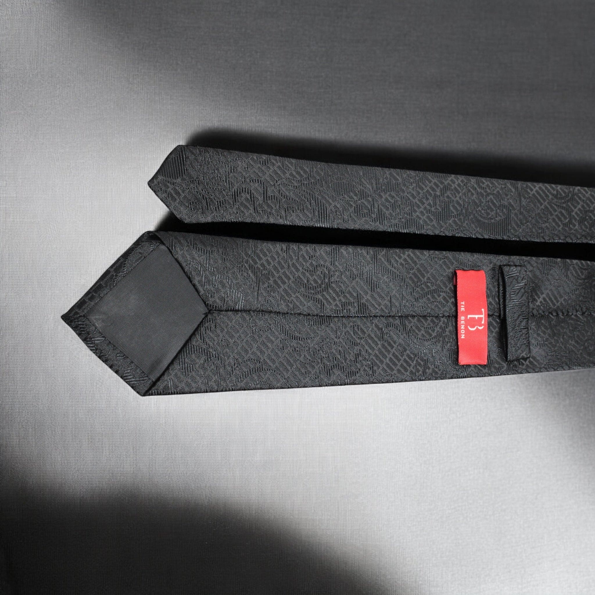 Black patterned tie with a red label on a gray background