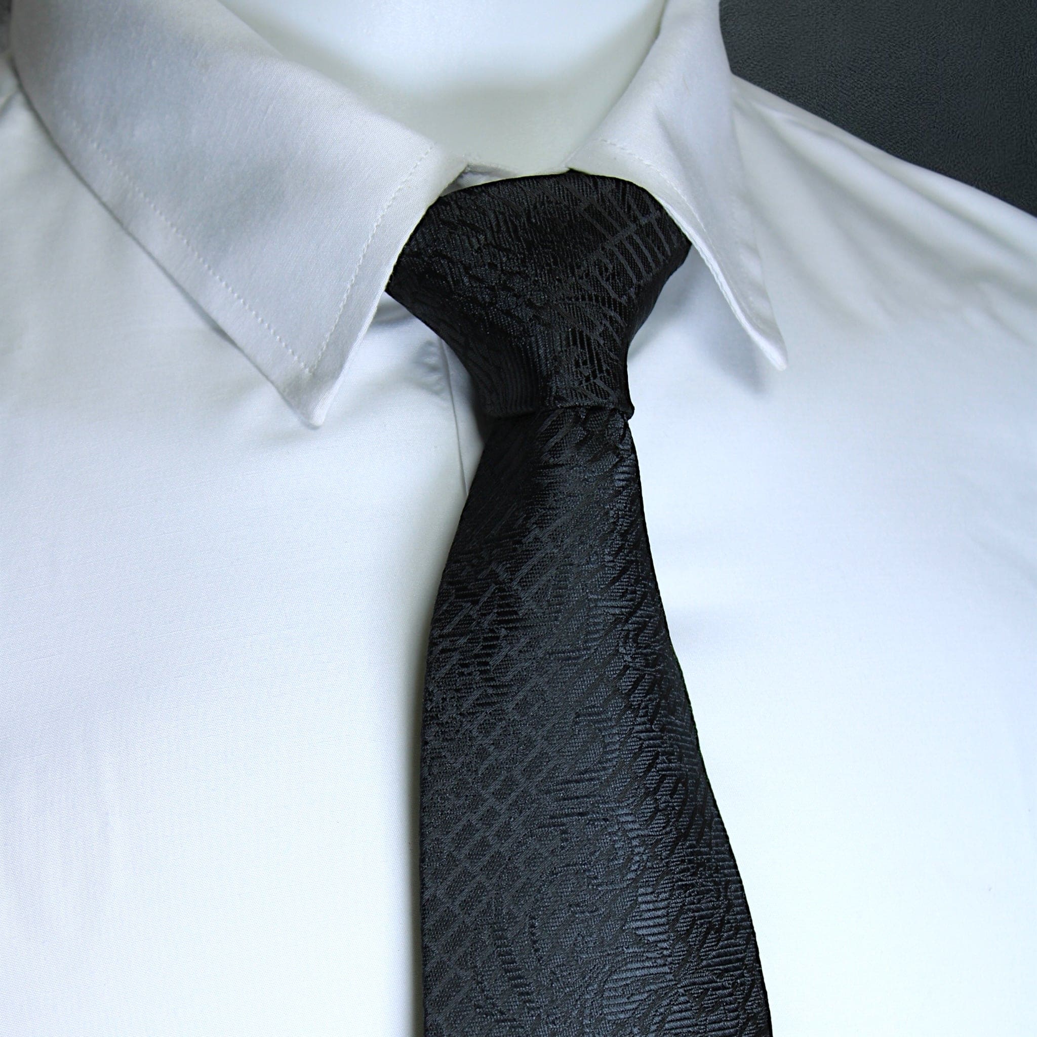 Black patterned tie on a white shirt against a black background