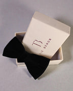 Black bow tie in a branded box on a gray background