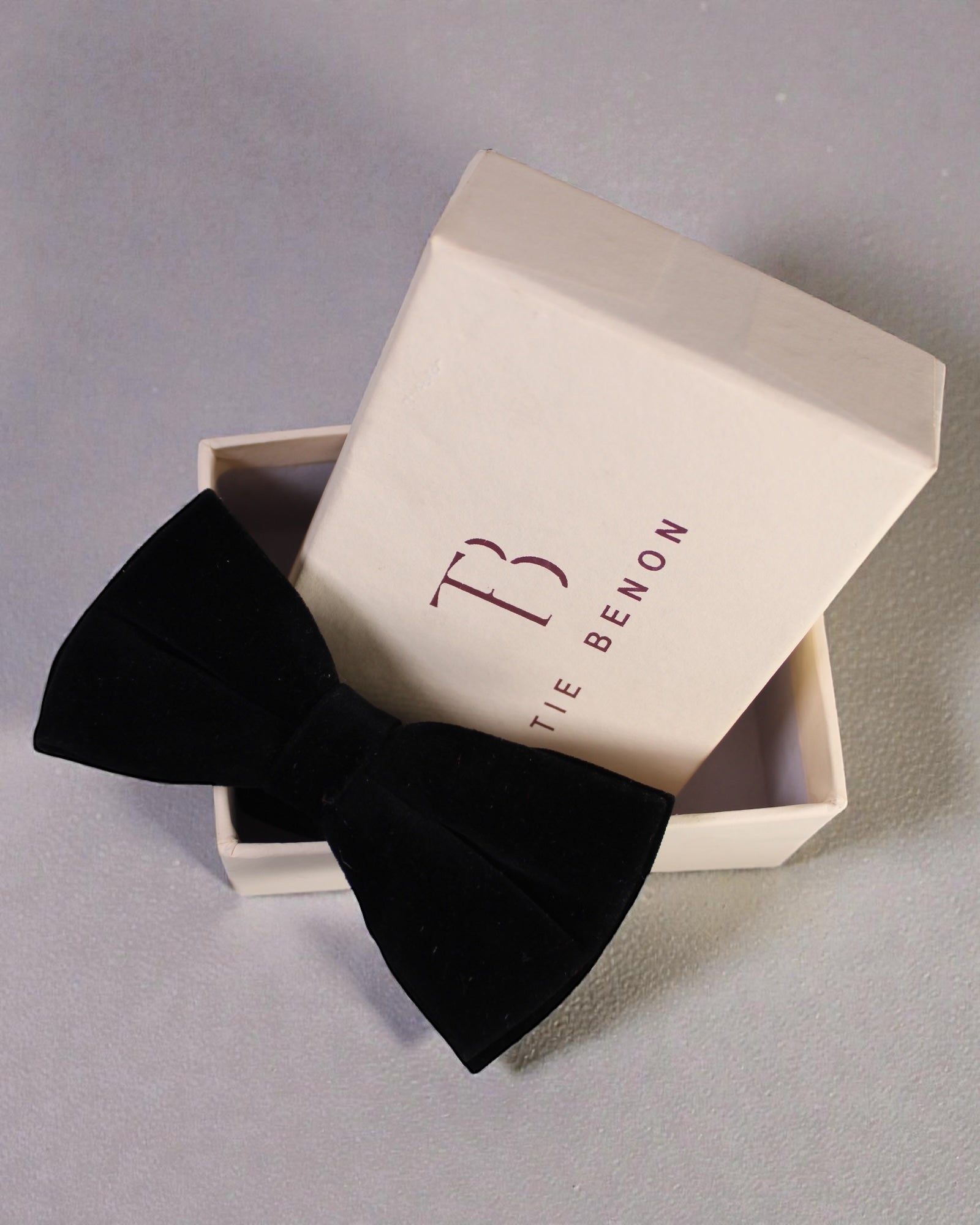 Black bow tie in a branded box on a gray background