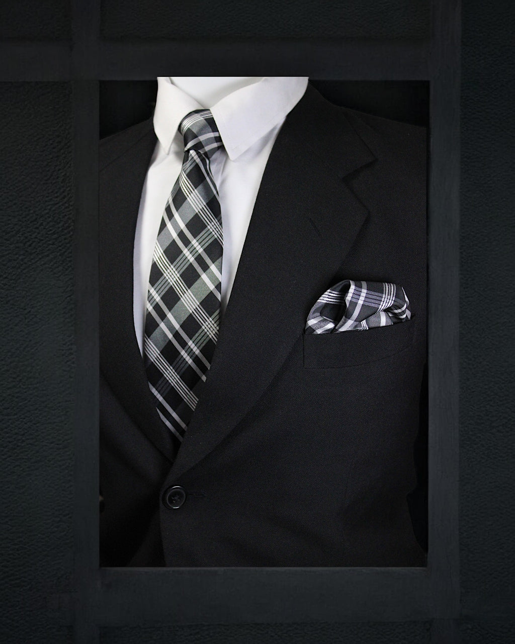 Black suit with plaid tie and pocket square on a dark background
