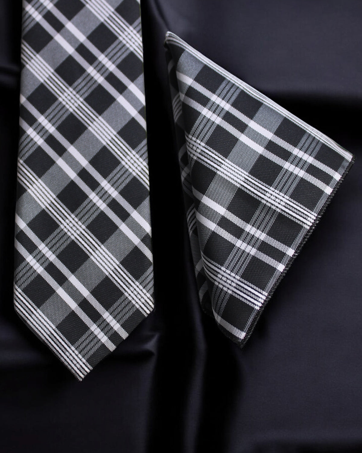 Black and white plaid tie and pocket square on a dark fabric background