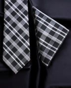 Black and white plaid tie and pocket square on a dark fabric background