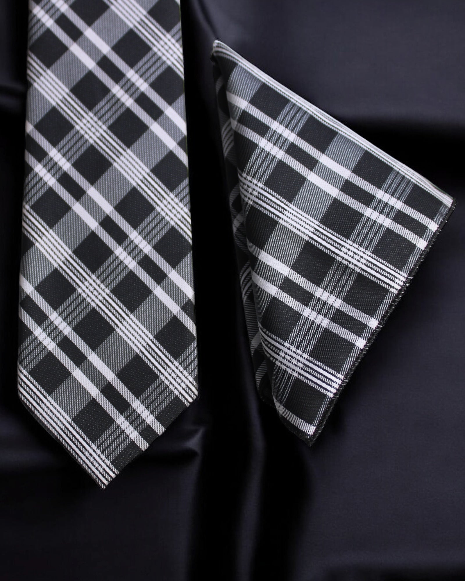 Black and white plaid tie and pocket square on a dark fabric background