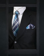 Black suit with white shirt, blue plaid tie, and matching pocket square on a dark background