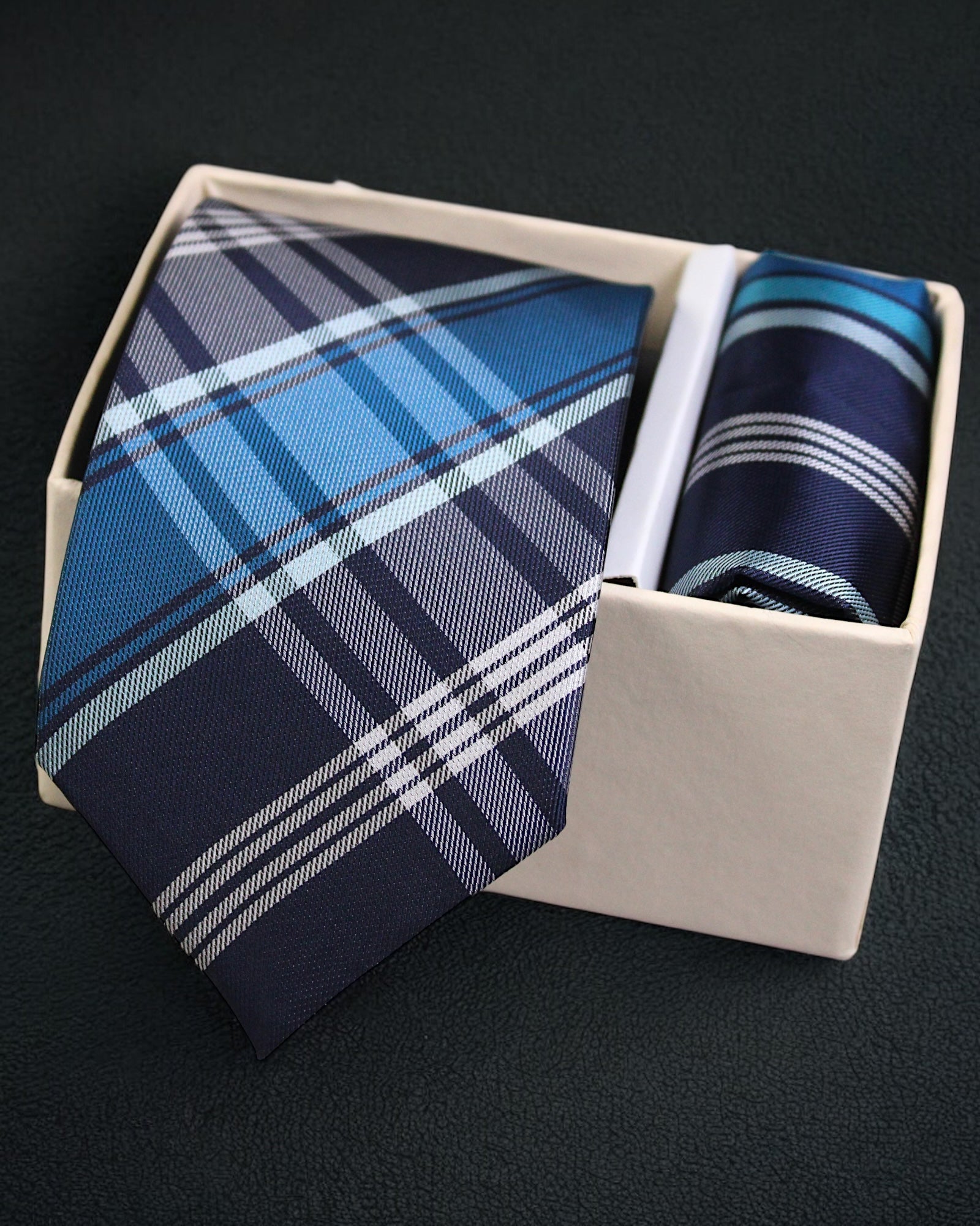 Blue plaid tie and pocket square set in a box on a black background