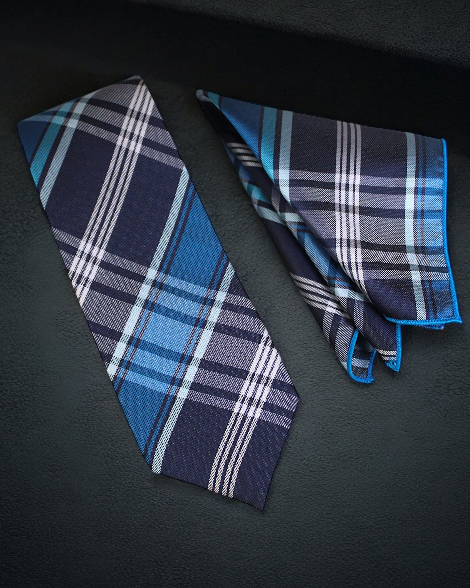 Blue plaid tie and pocket square on a dark surface