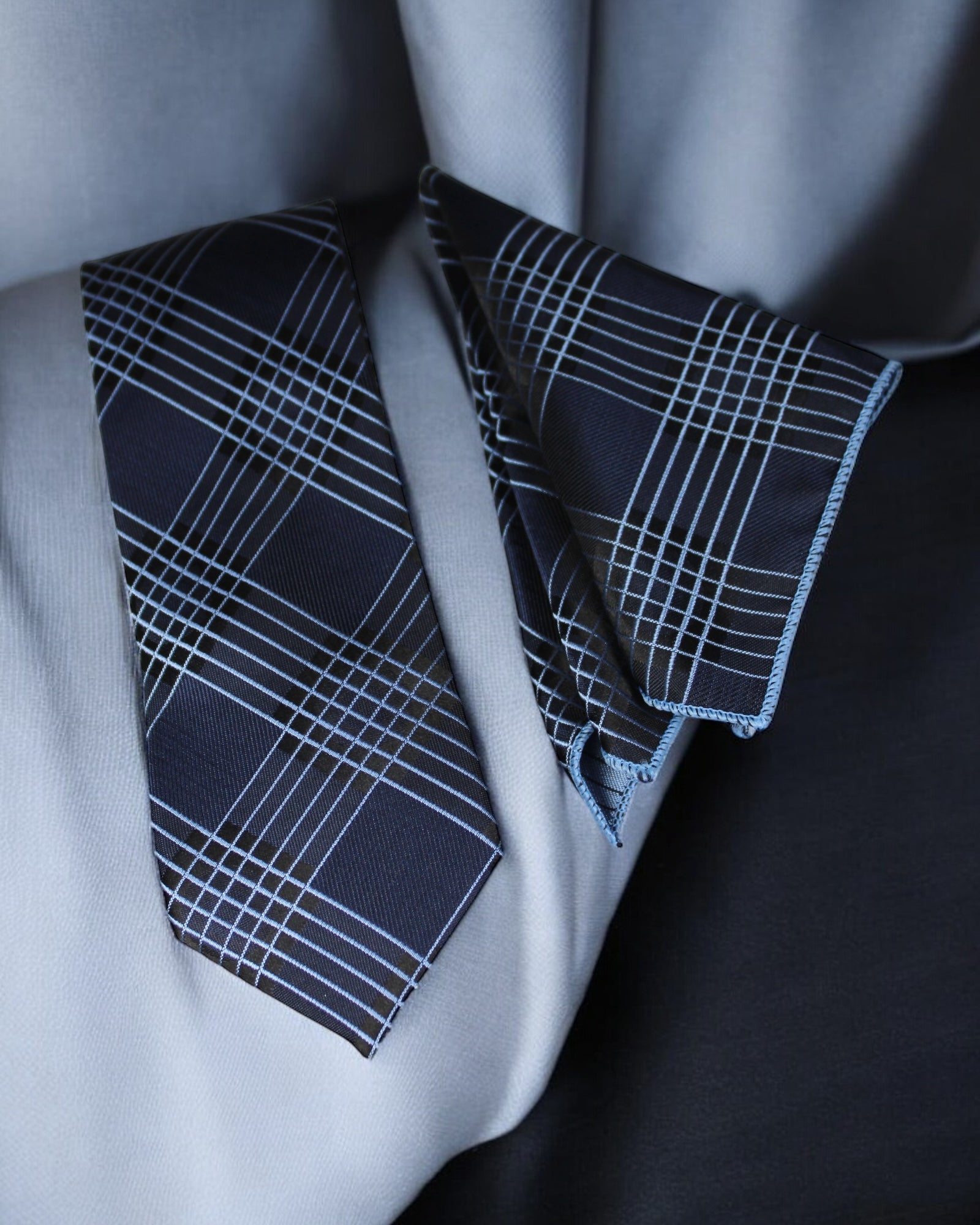 Navy plaid tie and pocket square on a light gray shirt against a dark background Tie Benon