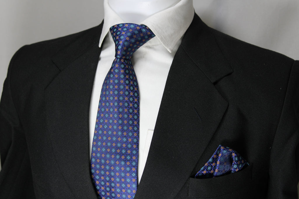 A blue multicolor geometric tie with a matching pocket square displayed on a mannequin wearing a black suit and a white shirt.