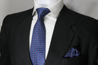 A blue multicolor geometric tie with a matching pocket square displayed on a mannequin wearing a black suit and a white shirt.