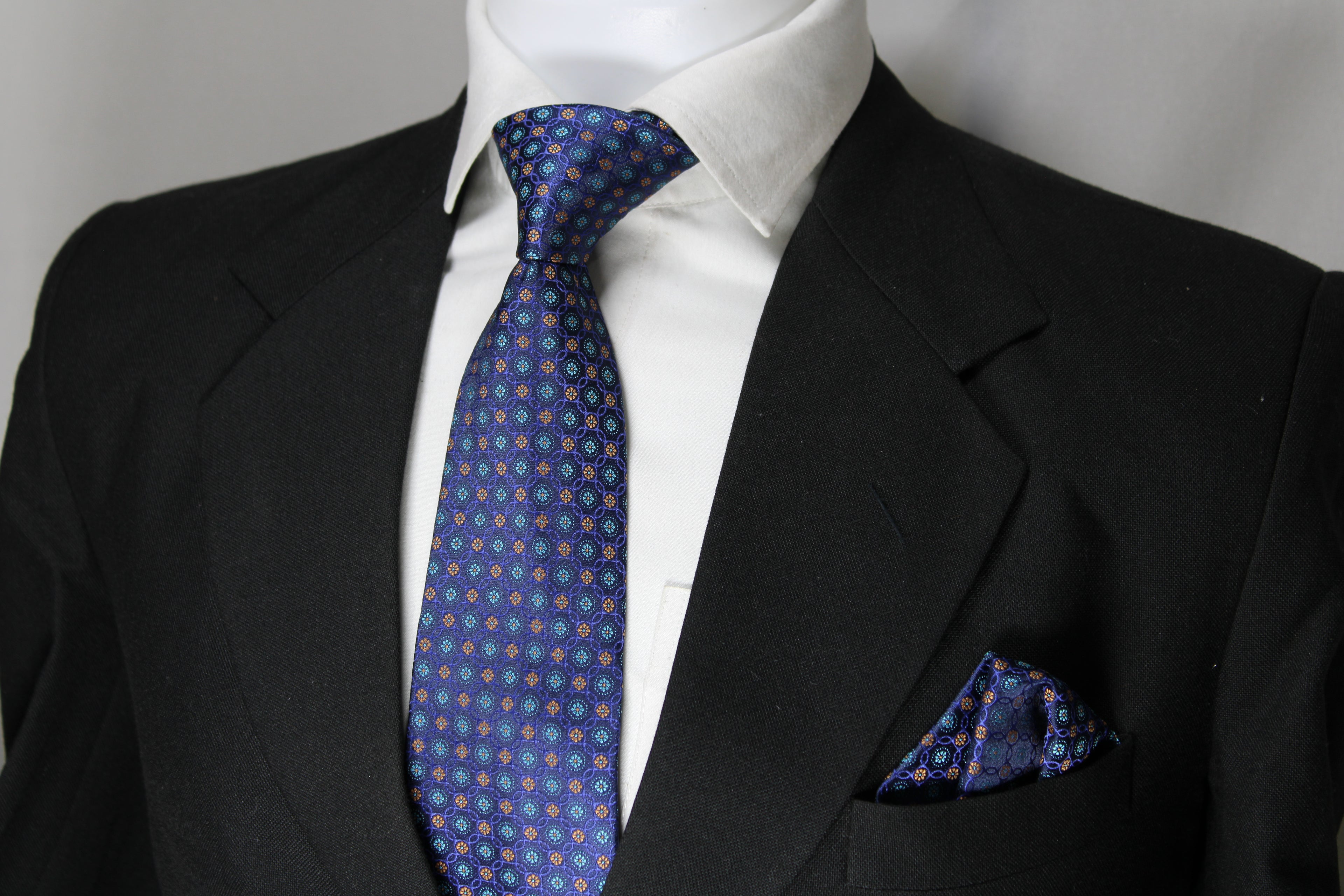 A blue multicolor geometric tie with a matching pocket square displayed on a mannequin wearing a black suit and a white shirt.