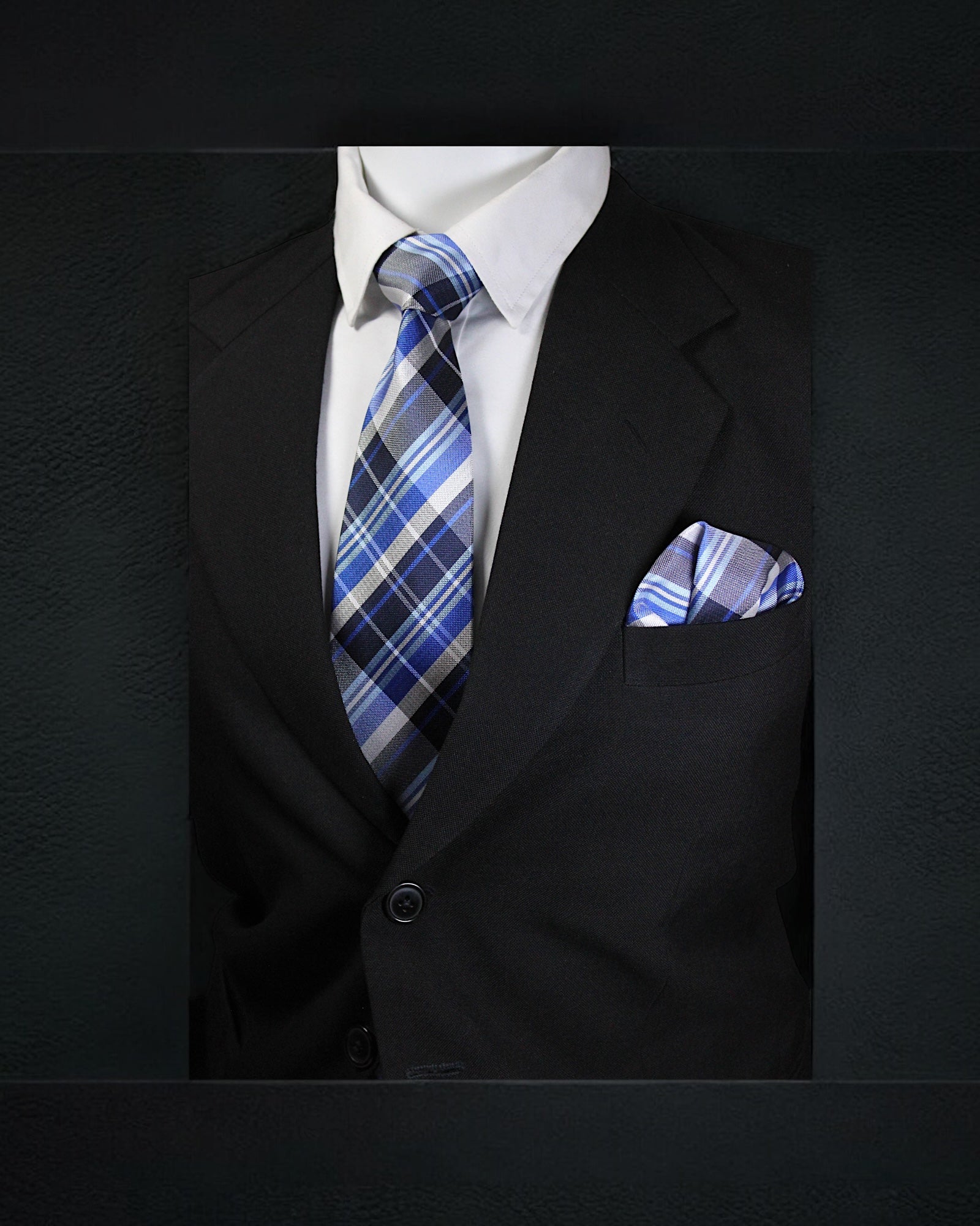 Black suit with a white shirt, blue plaid tie, and matching pocket square on a dark background