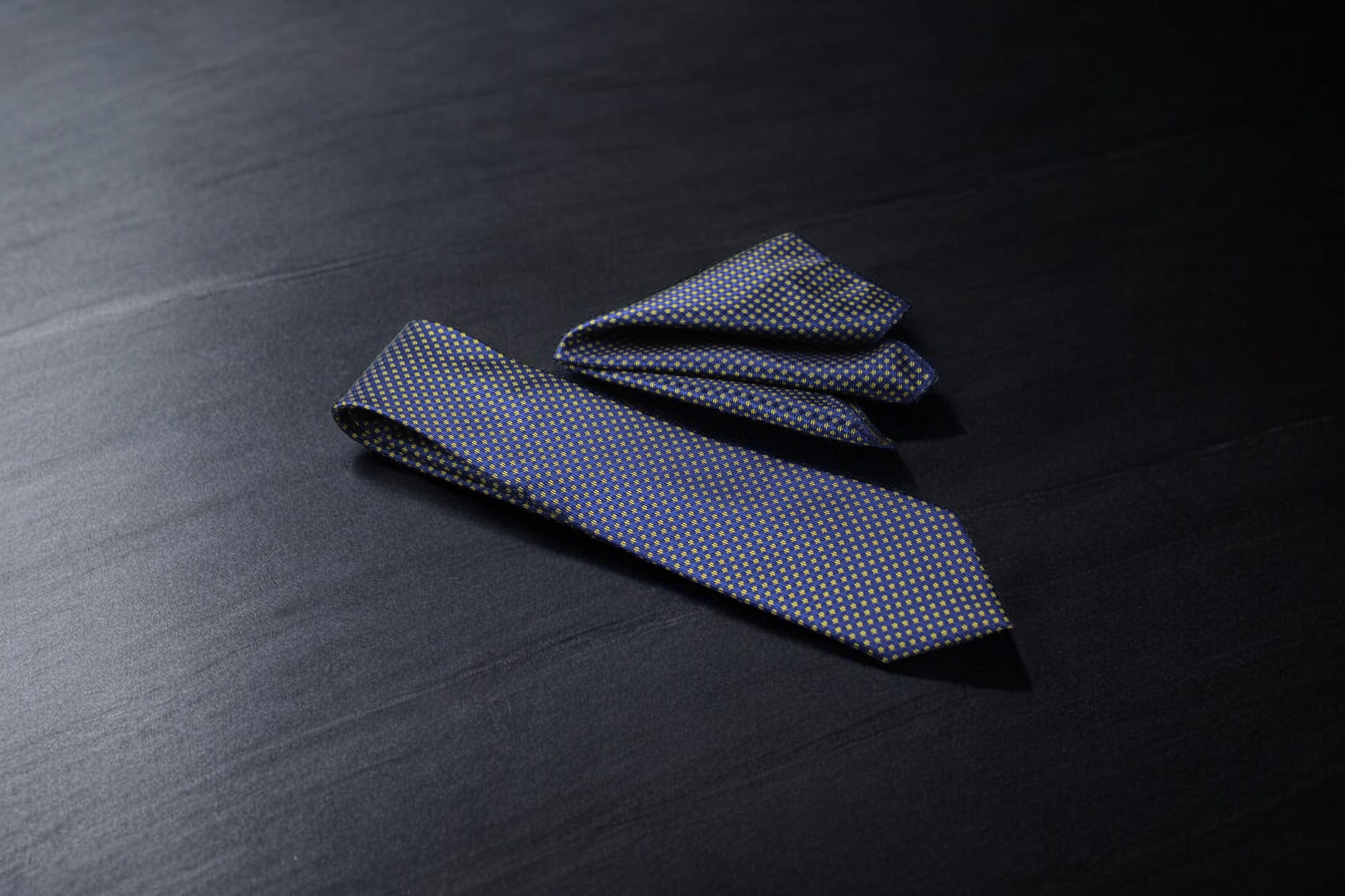 A blue and yellow dotted tie laid out flat on a dark surface.