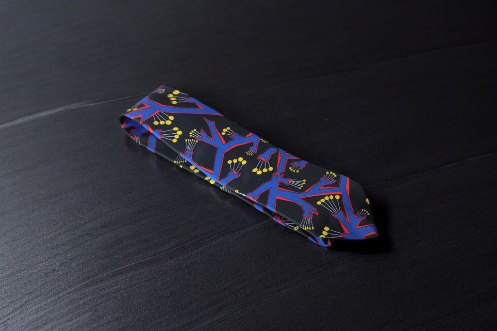 A black necktie with a bold geometric botanical pattern, laid out on a dark surface.