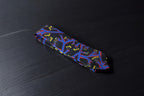 A black necktie with a bold geometric botanical pattern, laid out on a dark surface.