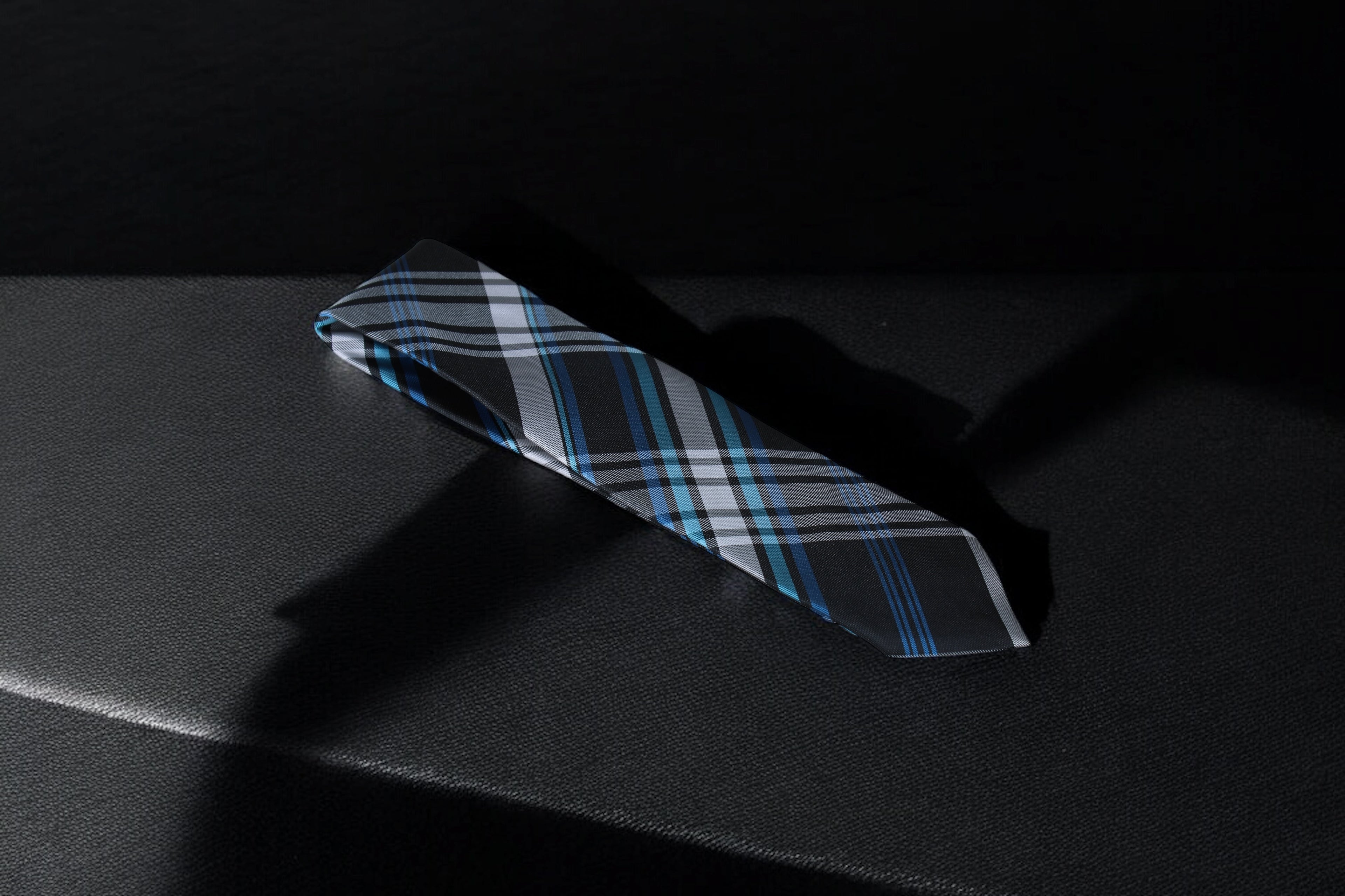 A checkered tie with navy, blue, and silver colors, lying flat on a dark surface.