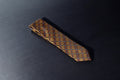 A brown and gold geometric plaid tie laid out on a dark surface.