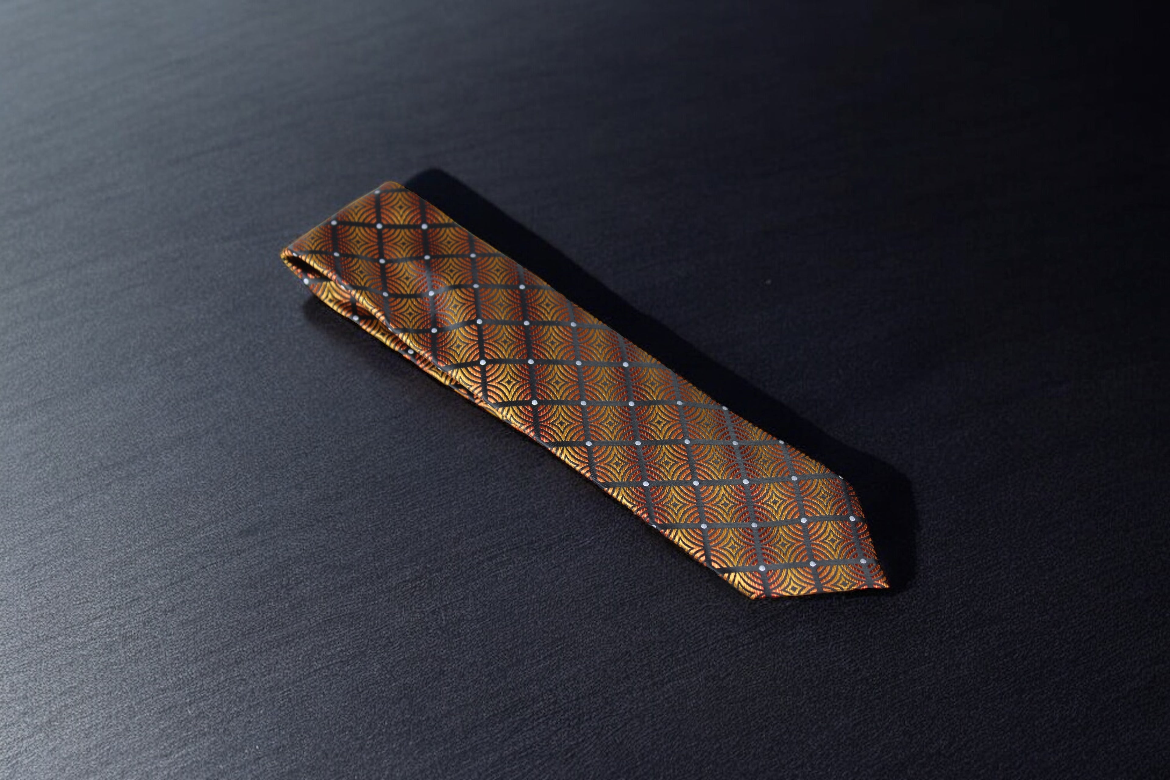 A brown and gold geometric plaid tie laid out on a dark surface.