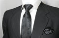 A black floral tie and pocket square set displayed on a mannequin wearing a black suit and white shirt.