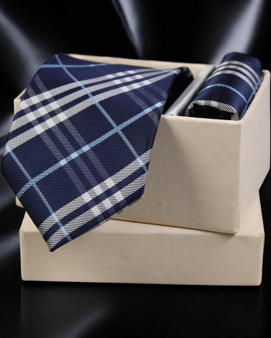 Navy and white plaid tie and pocket square set on a beige stand with a dark background tie Benon