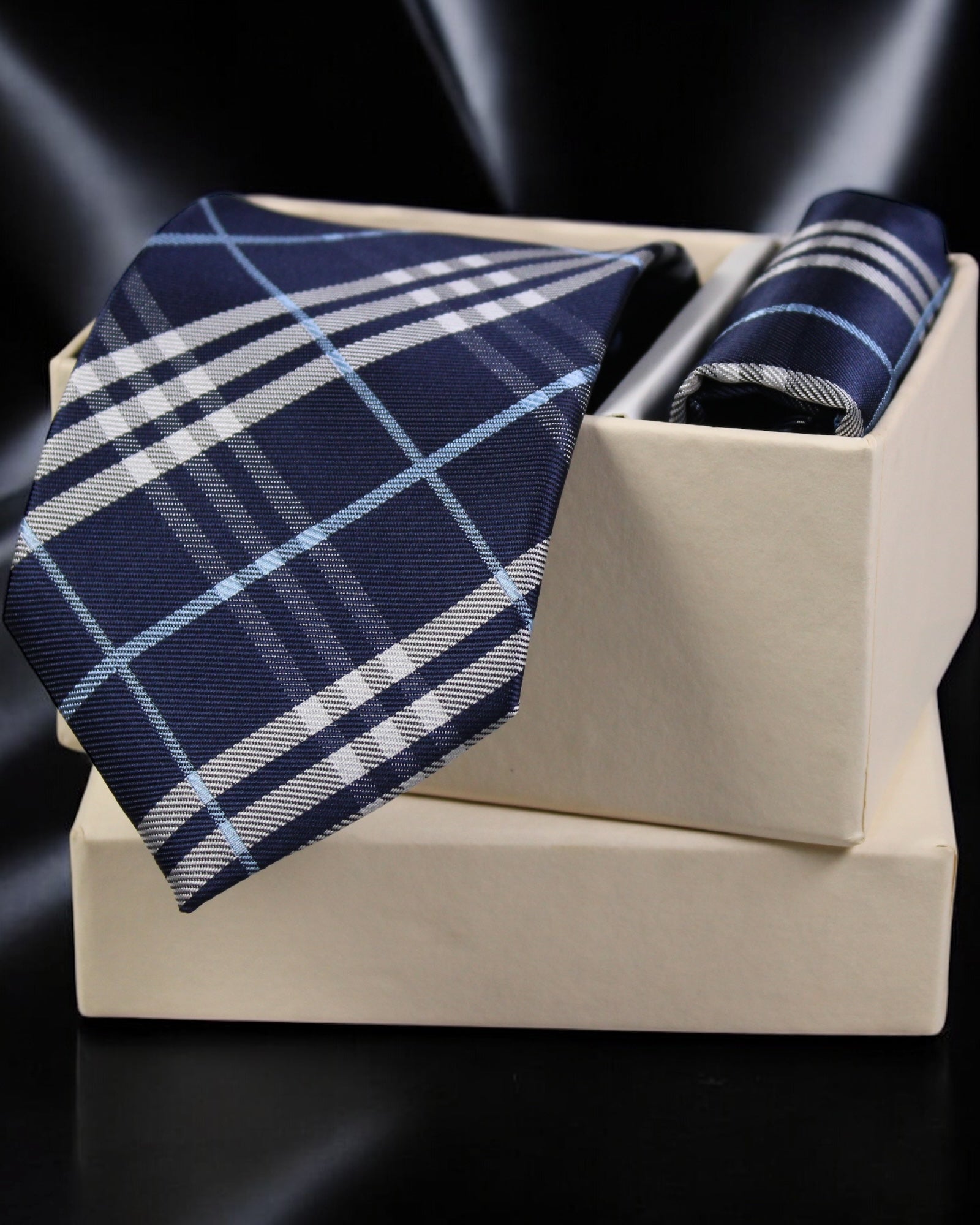Navy and white plaid tie and pocket square set on a beige stand with a dark background tie Benon