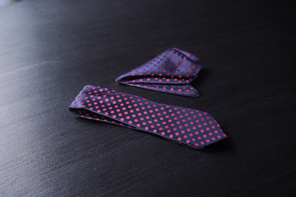 A navy and maroon polka tie laid out flat on a dark surface.