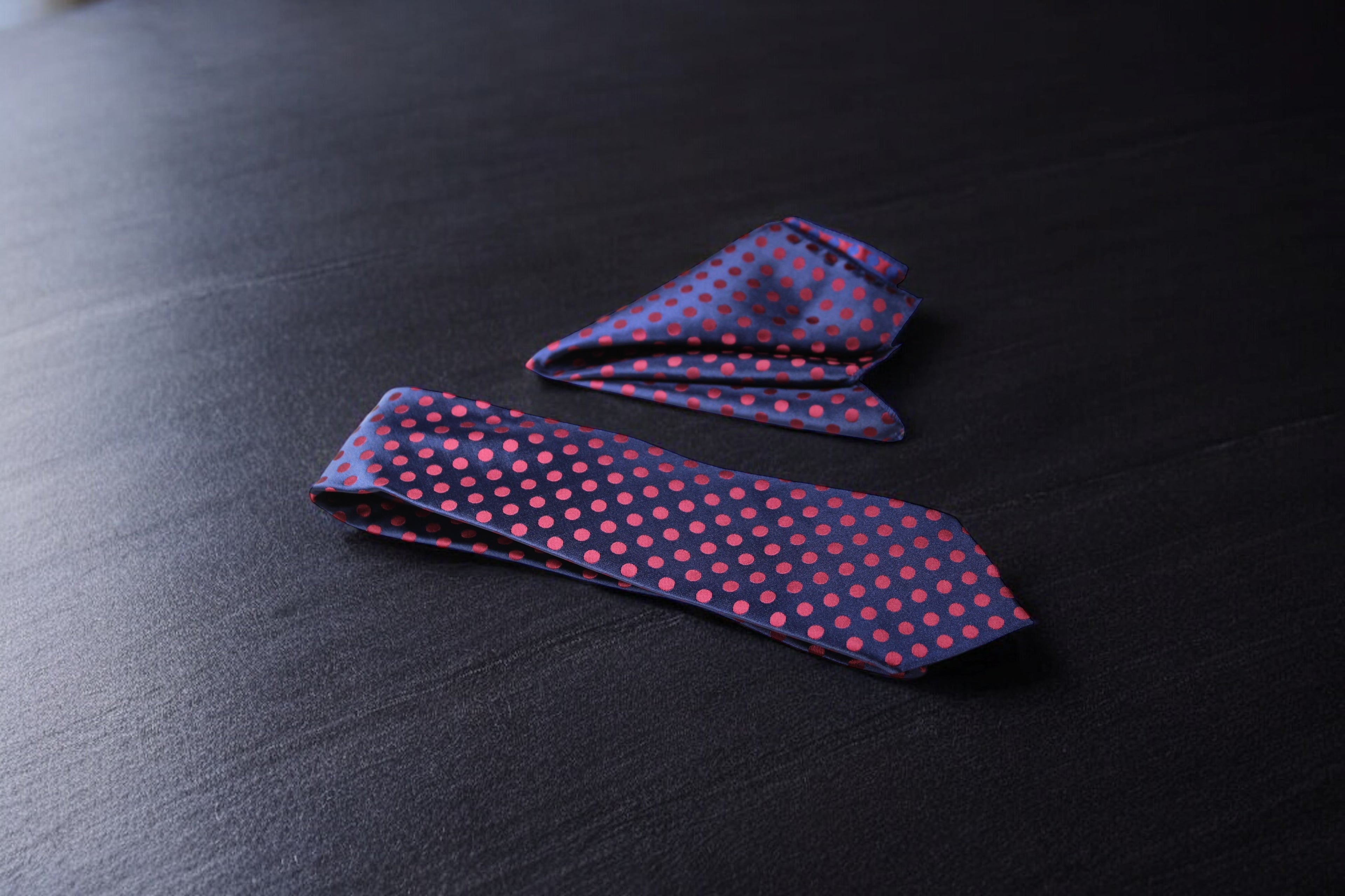 A navy and maroon polka tie laid out flat on a dark surface.