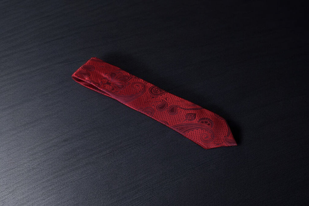 A red necktie with a paisley pattern laid out on a dark surface.