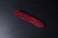 A red necktie with a paisley pattern laid out on a dark surface.