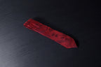 A red necktie with a paisley pattern laid out on a dark surface.