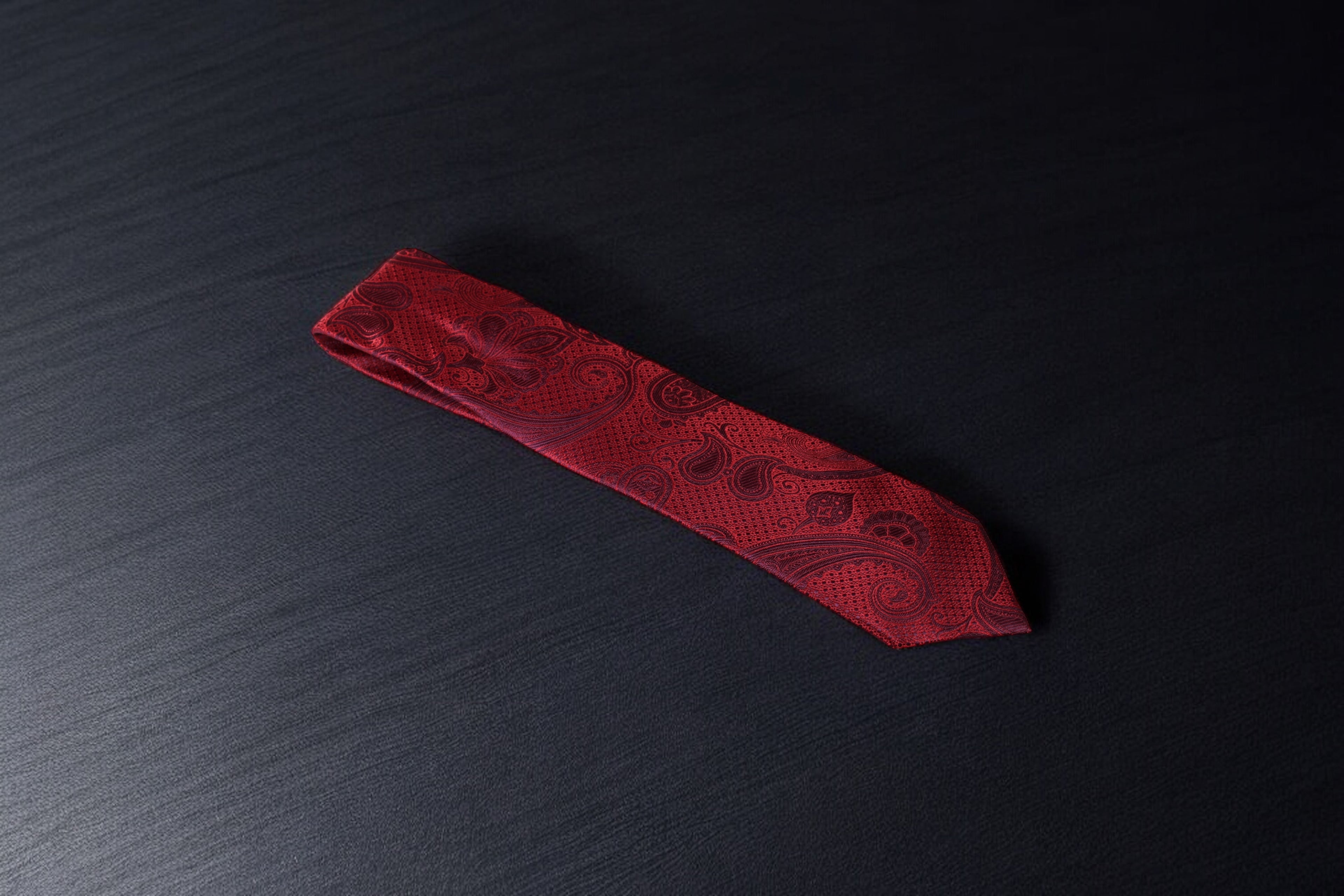 A red necktie with a paisley pattern laid out on a dark surface.