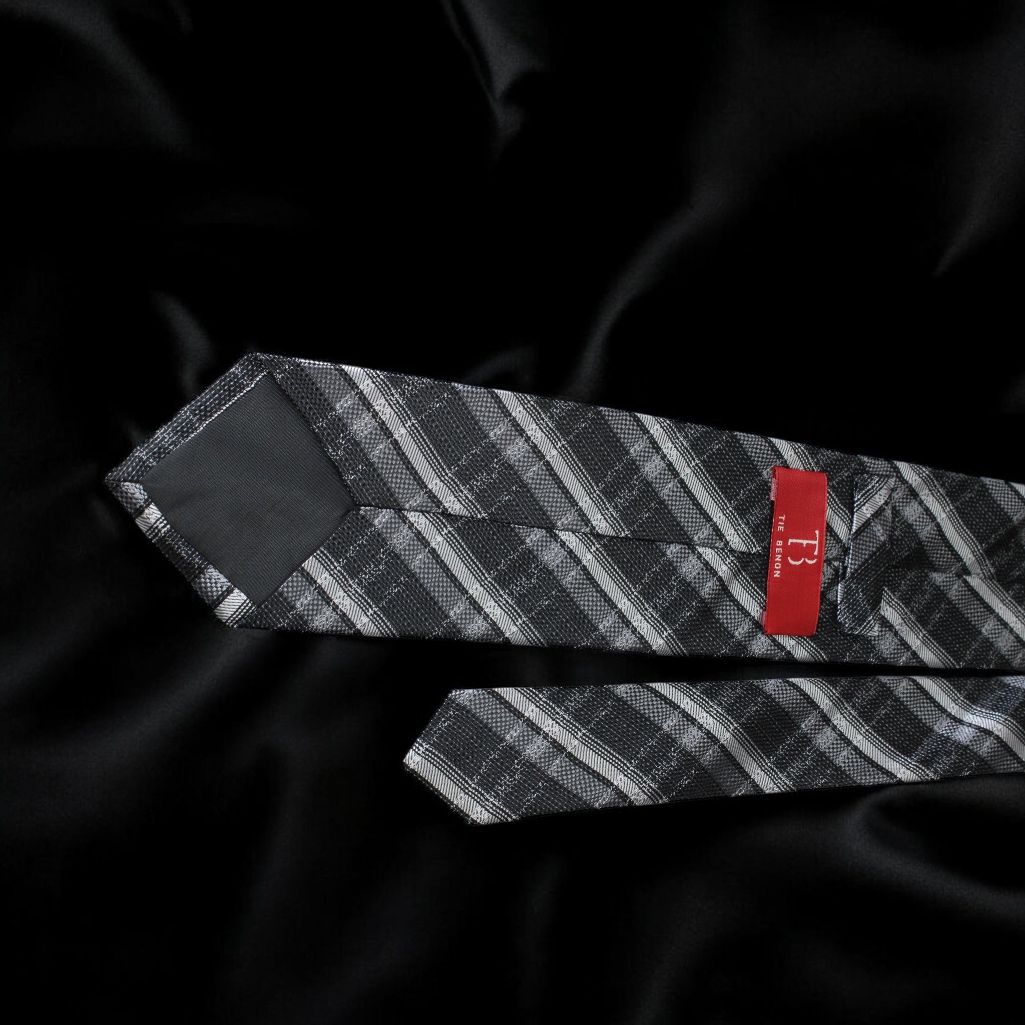 Black and gray patterned tie with a red label on a black satin background