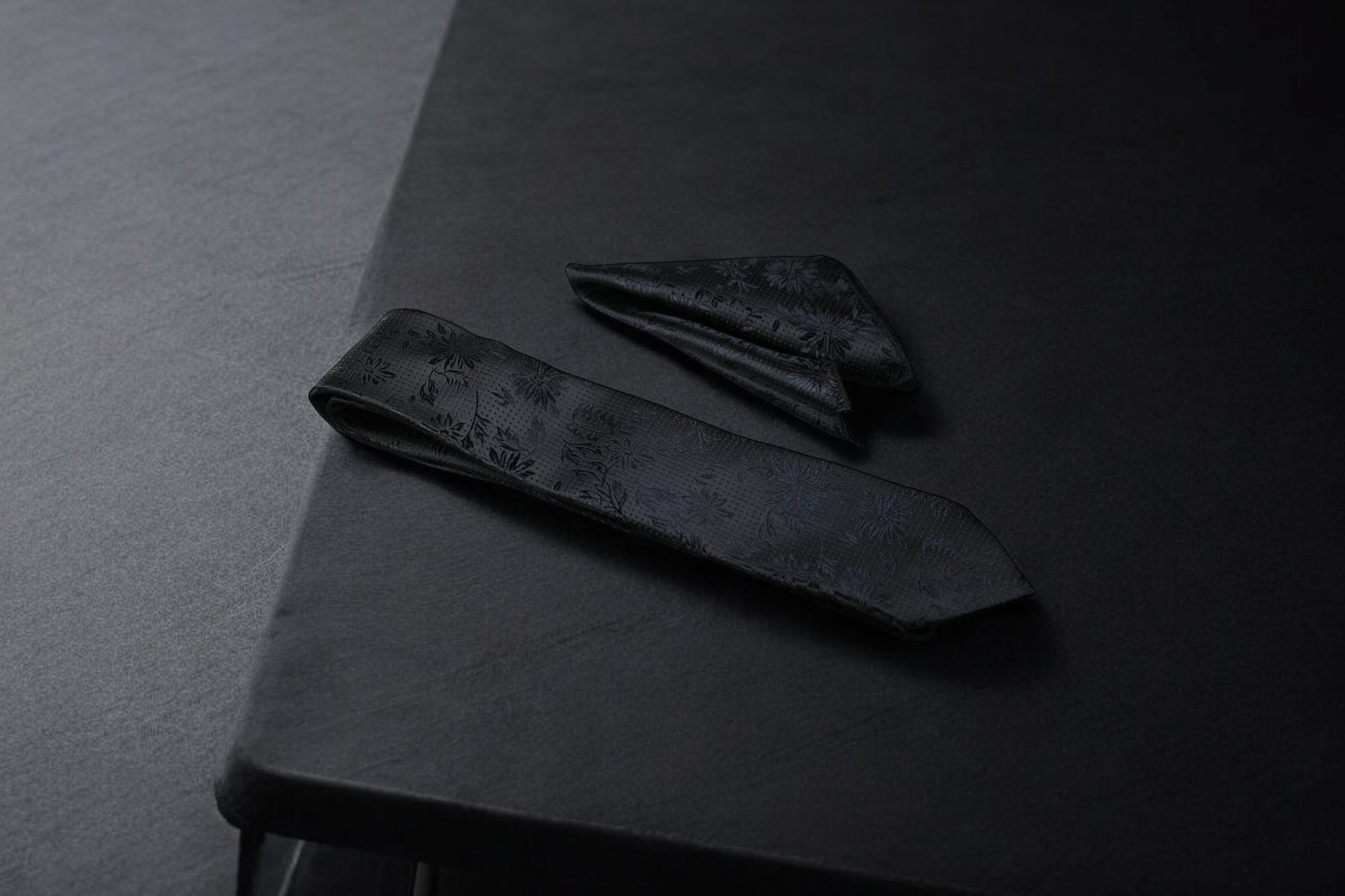 A black floral tie and pocket square set on a dark background.
