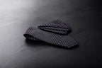 A dark purple geometric patterned tie and pocket square set laid out on a dark surface.