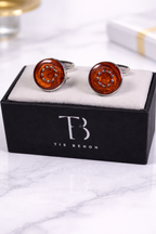 Brown round cufflinks on a black box with 'Tie Benon' branding on a marble surface.