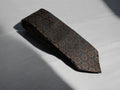 A black and brown geometric patterned tie laid out on a surface.