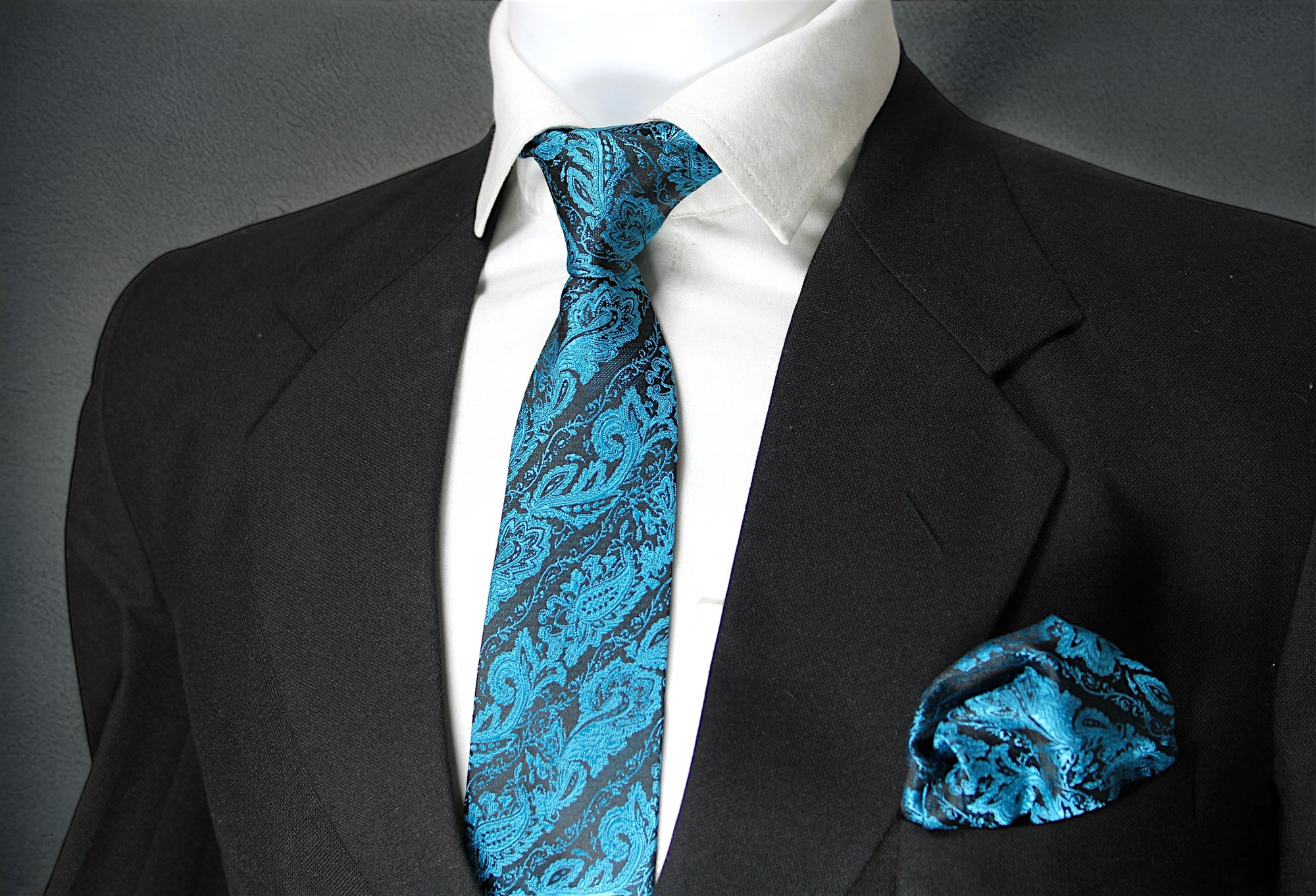 A blue paisley tie with a pocket square, displayed on a mannequin wearing a black suit and white shirt.