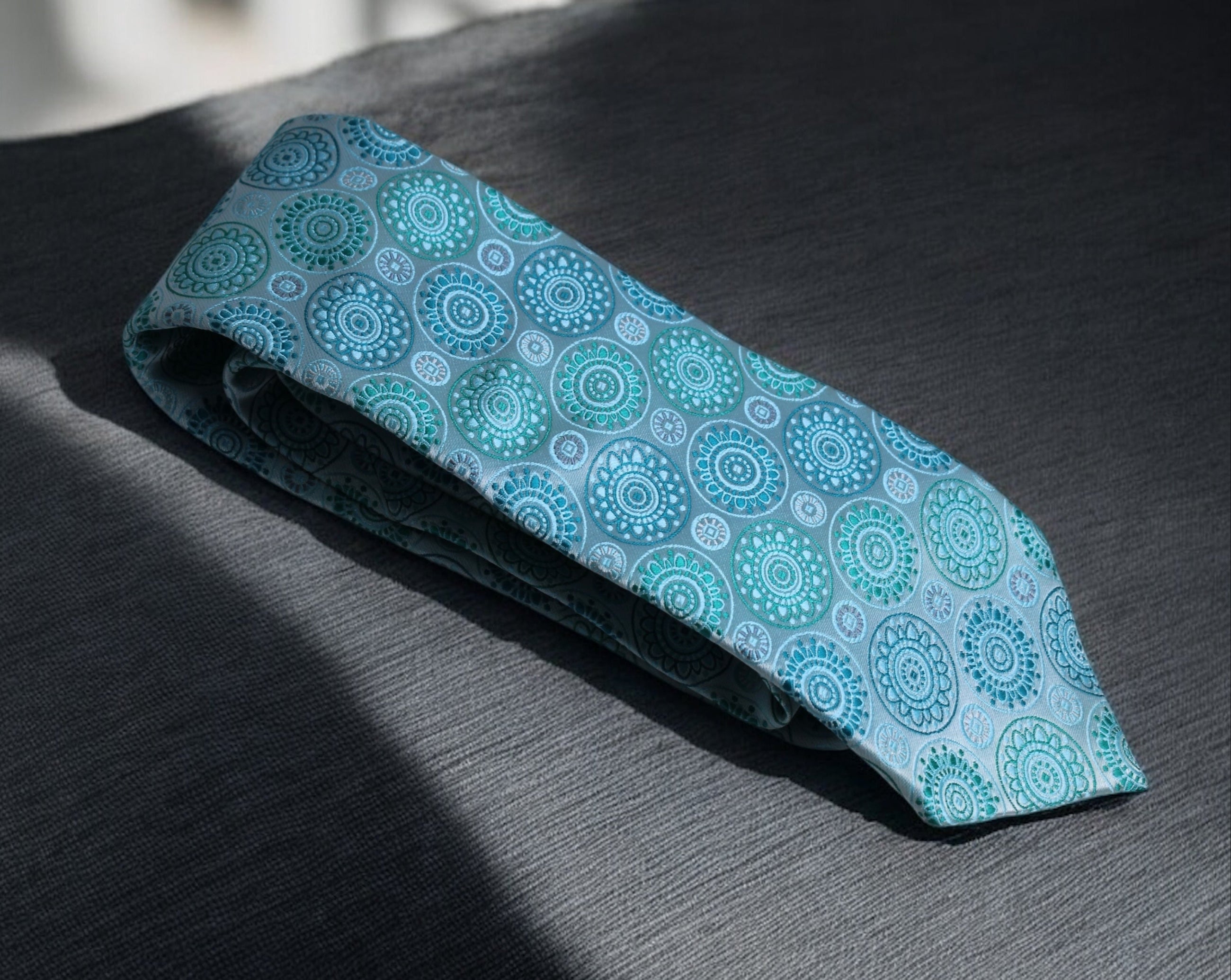 A necktie with a mandala pattern in blue and sea green colors laid out on a flat surface.