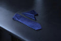 A dark blue geometric tie and a matching pocket square laid out on a dark surface.